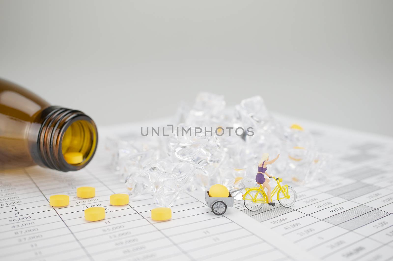 Woman is cycling and carry yellow pill on finance report have blur stack of ice and brown bottle as background.