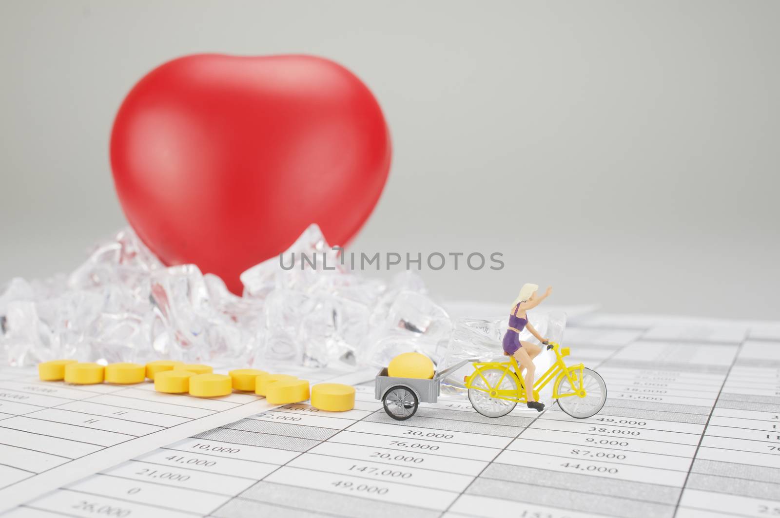 Woman is cycling and carry yellow pill on finance report have blur red heart on stack of ice as background.