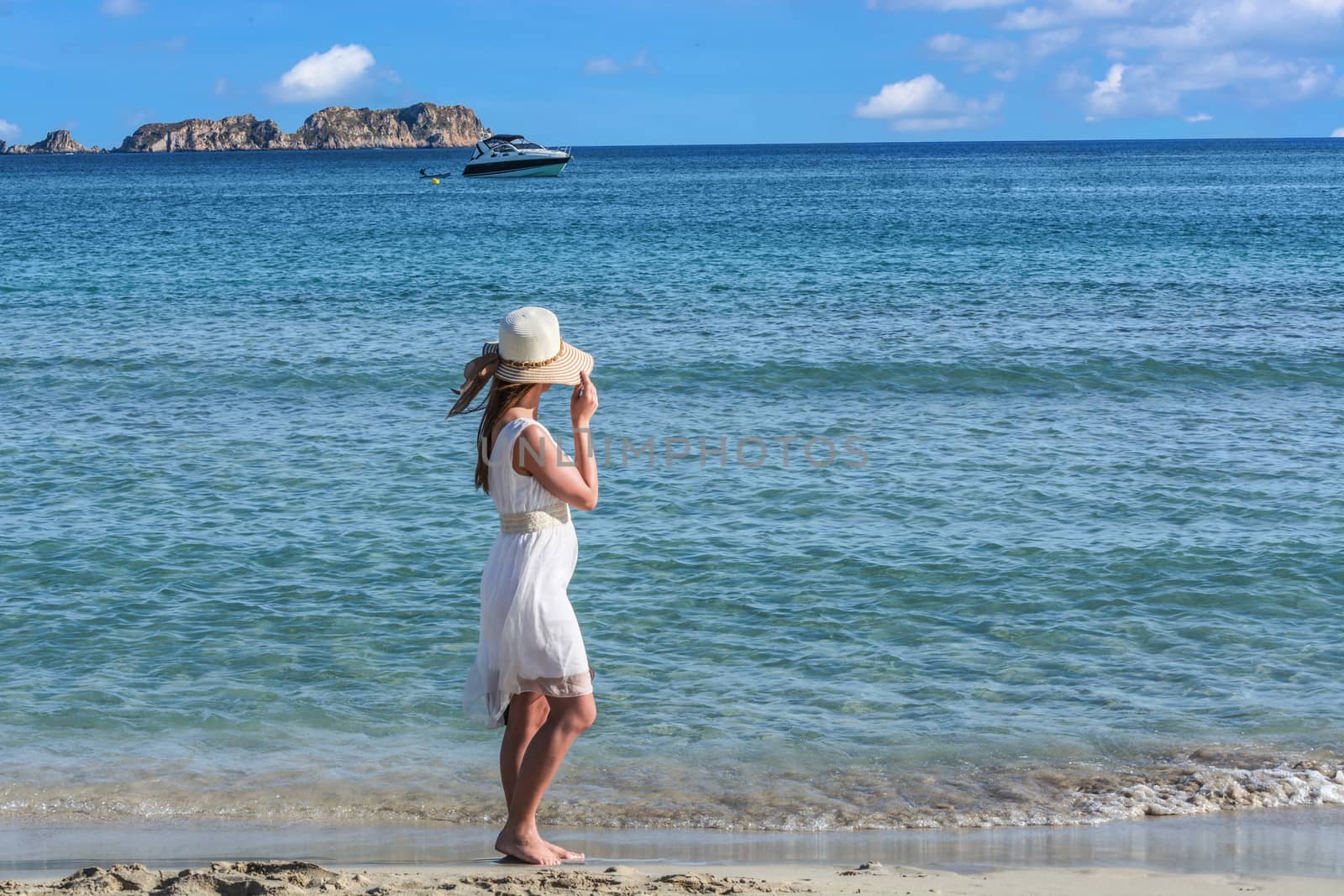 Young woman on the beach overlooking the sea in the background a motorboat.