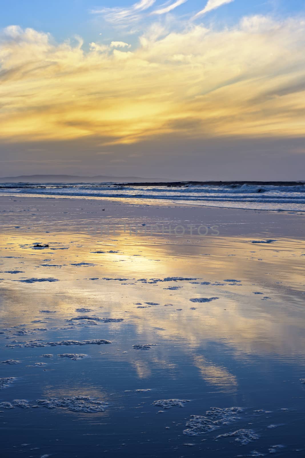 reflections and calm waves crashing onto the beach at ballybunion in ireland