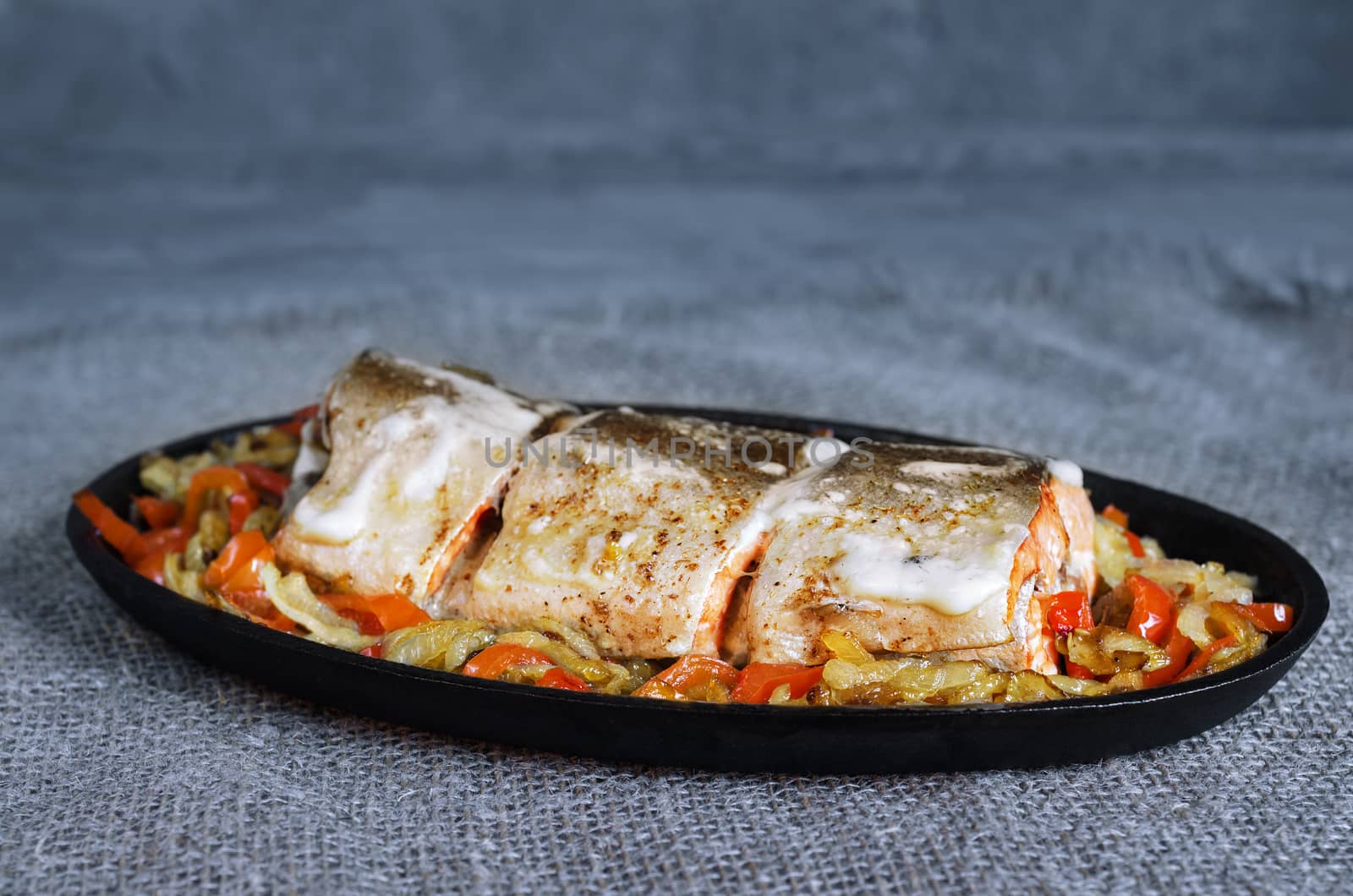 Salmon baked in mayonnaise with vegetables in a cast iron skillet and a gray-blue background. Rustic style