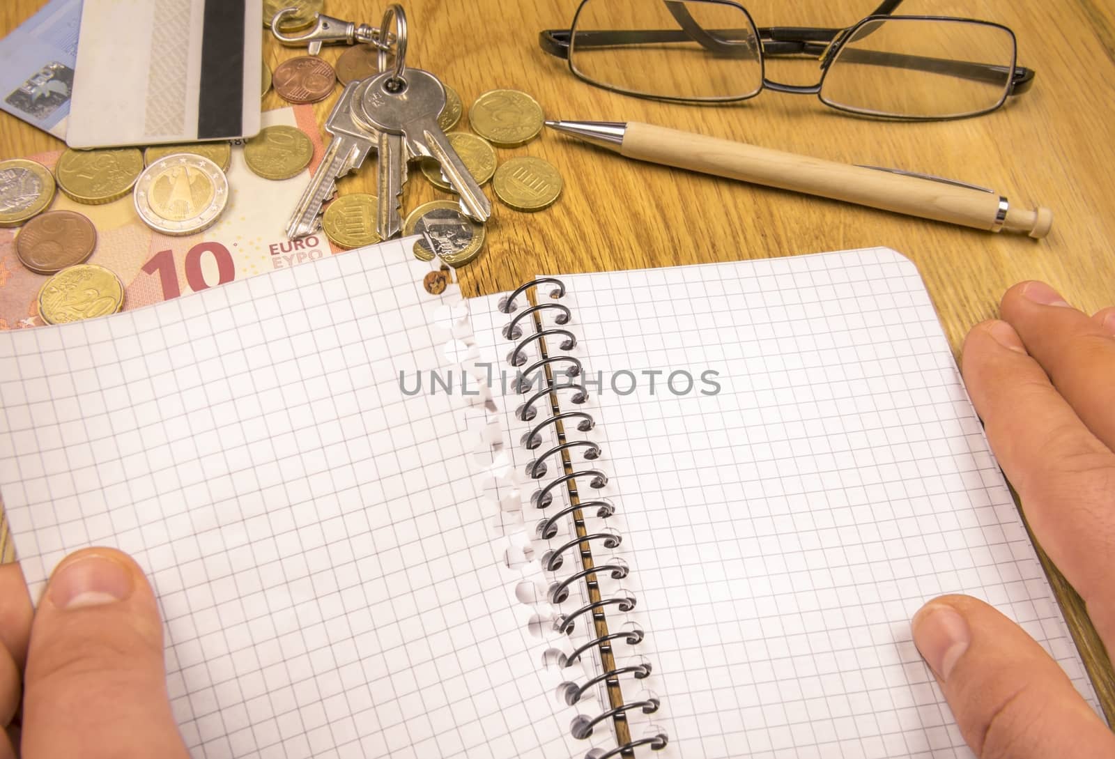 Conceptual image with a man's hand tearing a blank page from a spiral math notebook, money, keys and credit cards in the background.