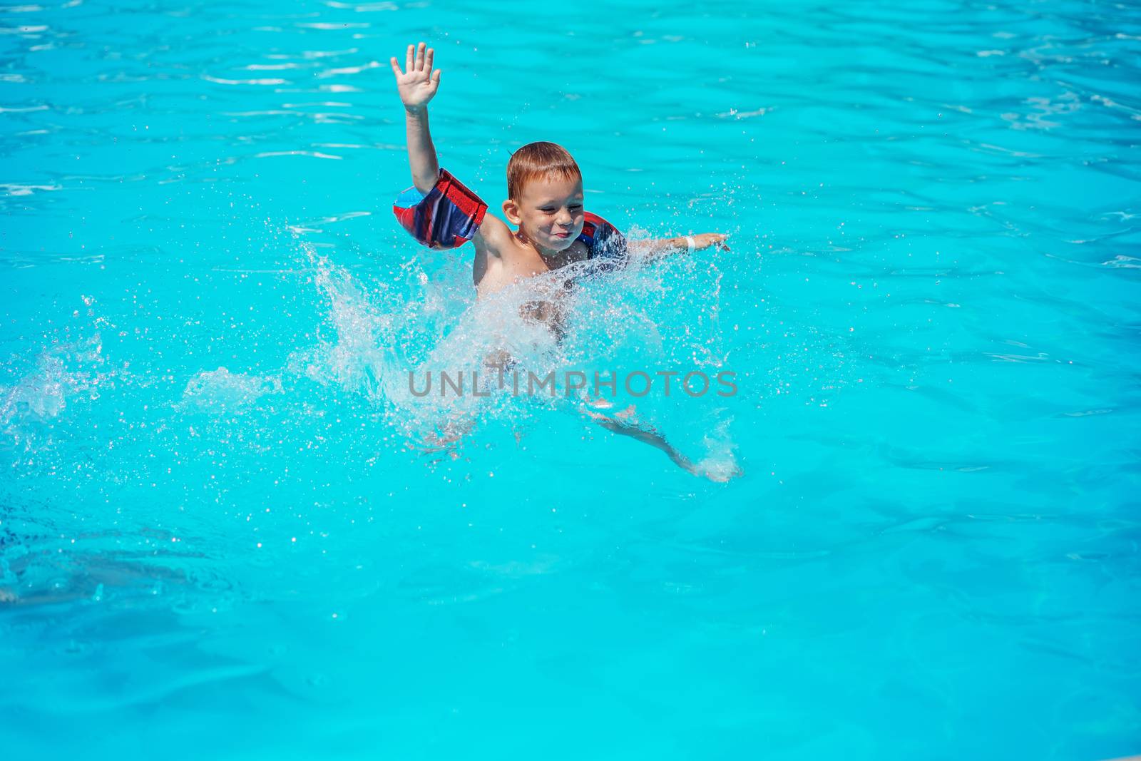 Happy kid playing in blue water of swimming pool. Little boy learning to swim. Summer vacations concept. Cute boy swimming in pool water. Child splashing and having fun in swimming pool