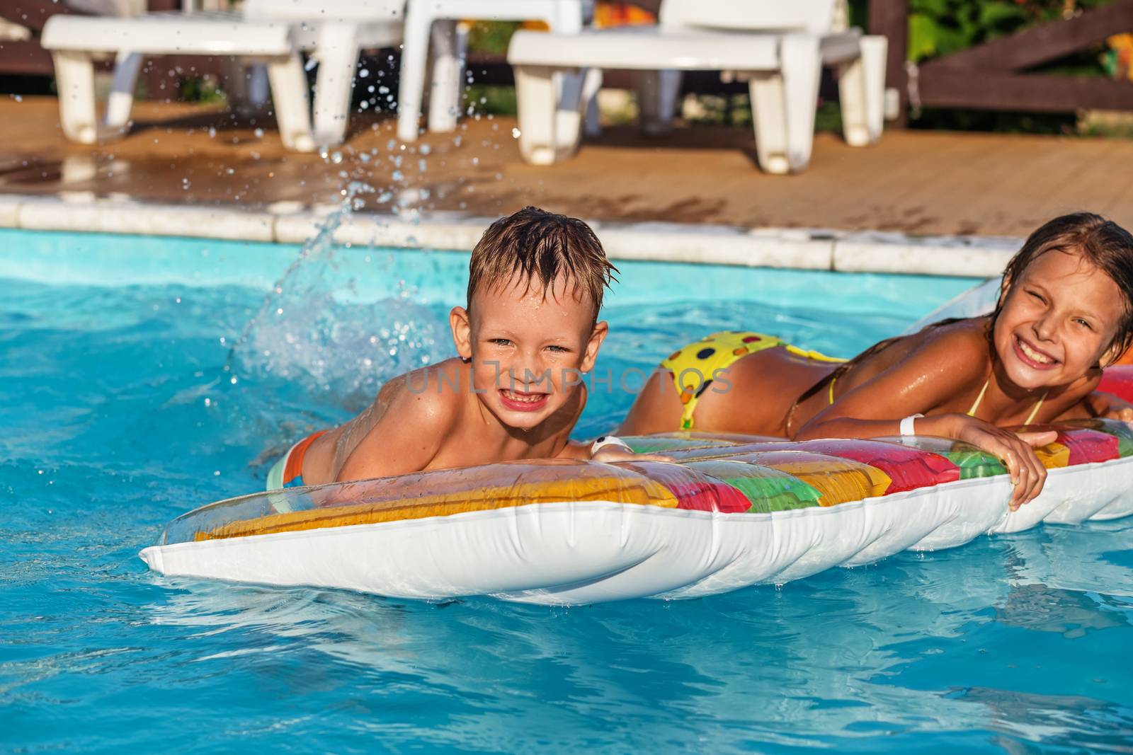 Little children on inflatable mattress in swimming pool. Smiling kids playing and having fun in swimming pool with air mattress. Boy and girl playing in water. Summer vacations concept.