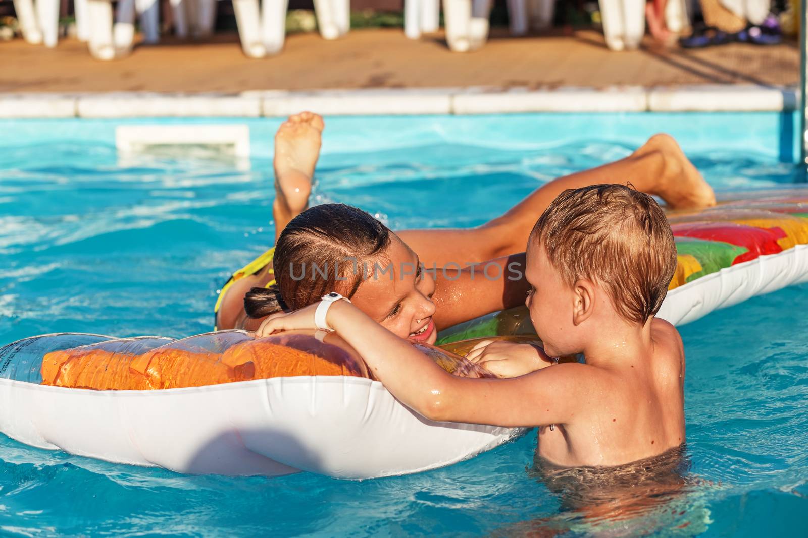 Little children on inflatable mattress in swim pool. Smiling kids playing and having fun in swimming pool with air mattress. Boy and girl playing in water. Summer vacations concept.