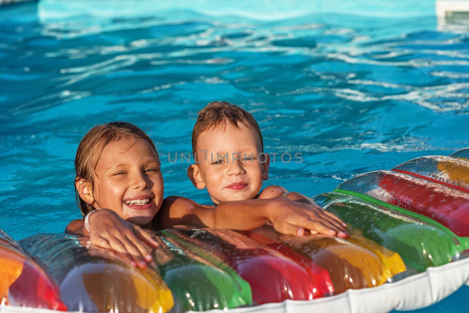 Little children on inflatable mattress in swimming pool. Smiling kids playing and having fun in swimming pool with air mattress. Boy and girl playing in water. Summer vacations concept.