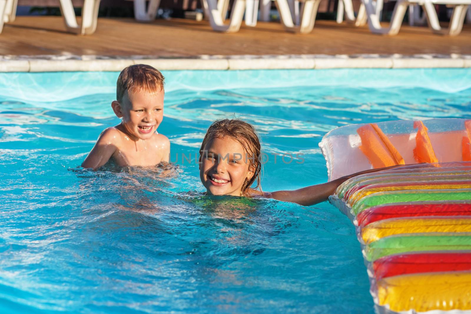 Happy kids playing in blue water of swimming pool. by natazhekova