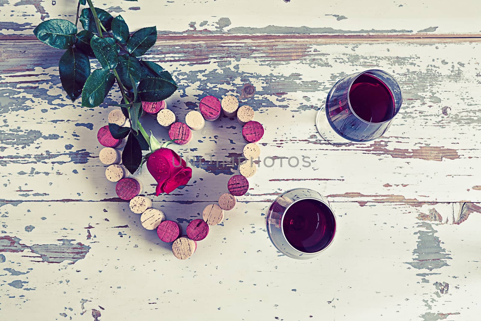 Two glasses of red wine a heart with a cork and a red rose in a vintage style.