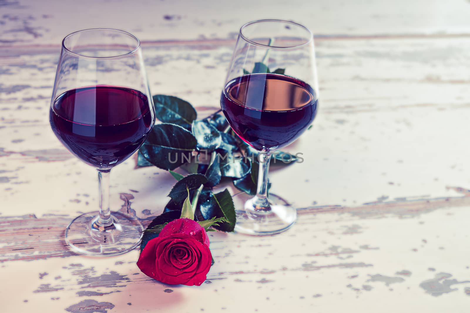 Two glasses of red wine and a red rose to celebrate a romantic day in vintage style