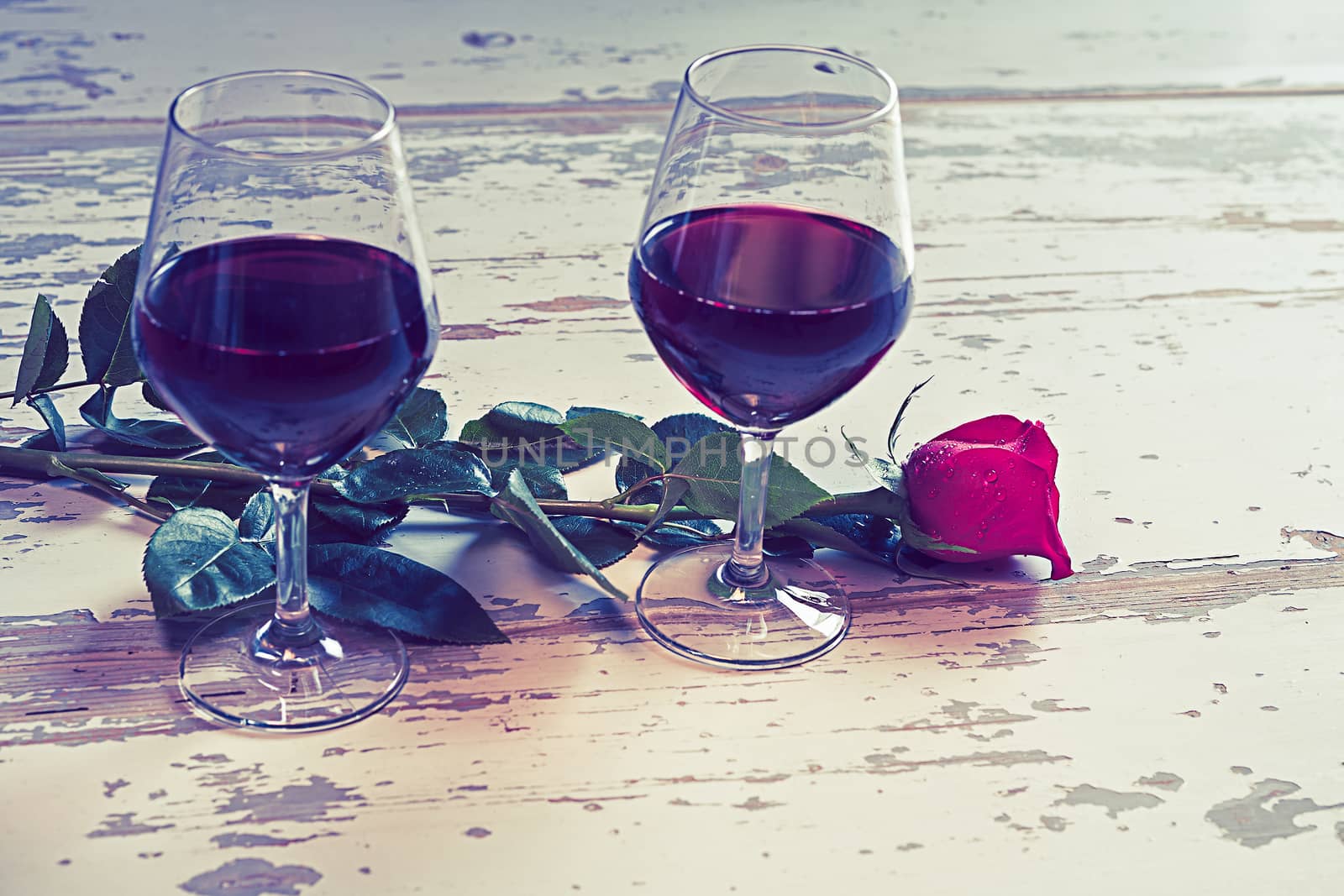 Two glasses of red wine and a red rose to celebrate a romantic day