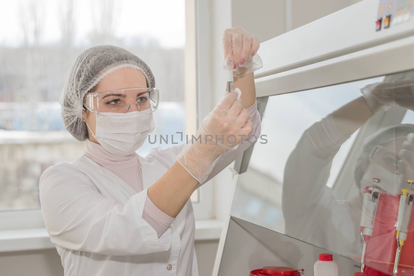 Woman scientist in a white protective clothing conducts research in a real lab