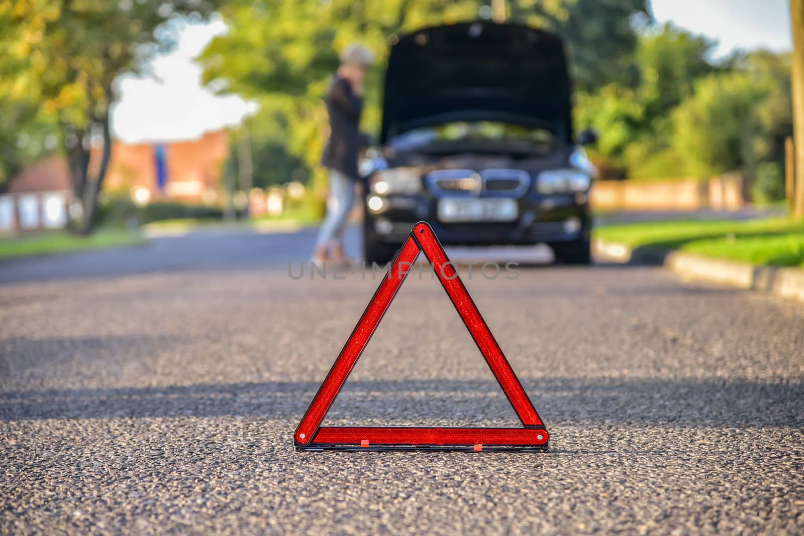 Broken down car with warning triangle,  waiting for assistance to arrive (shallow depth of field, the focus is on the triangle, the car is left out of focus).