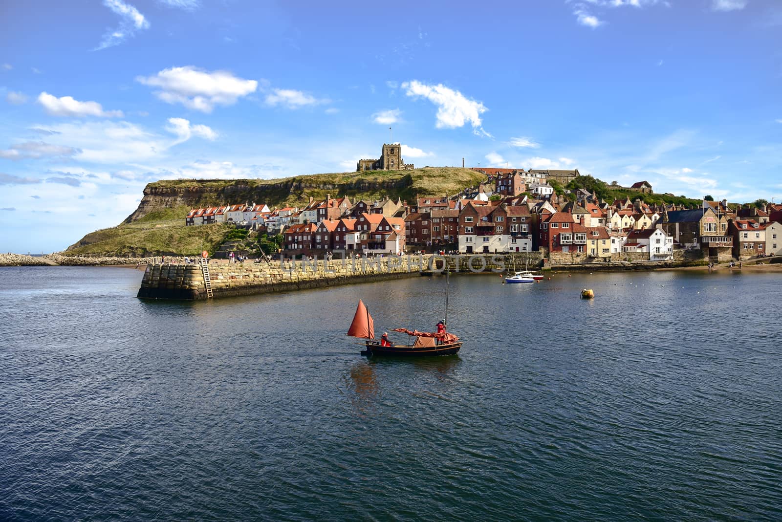 View of boat returning to Whitby Harbour and gothic church in background