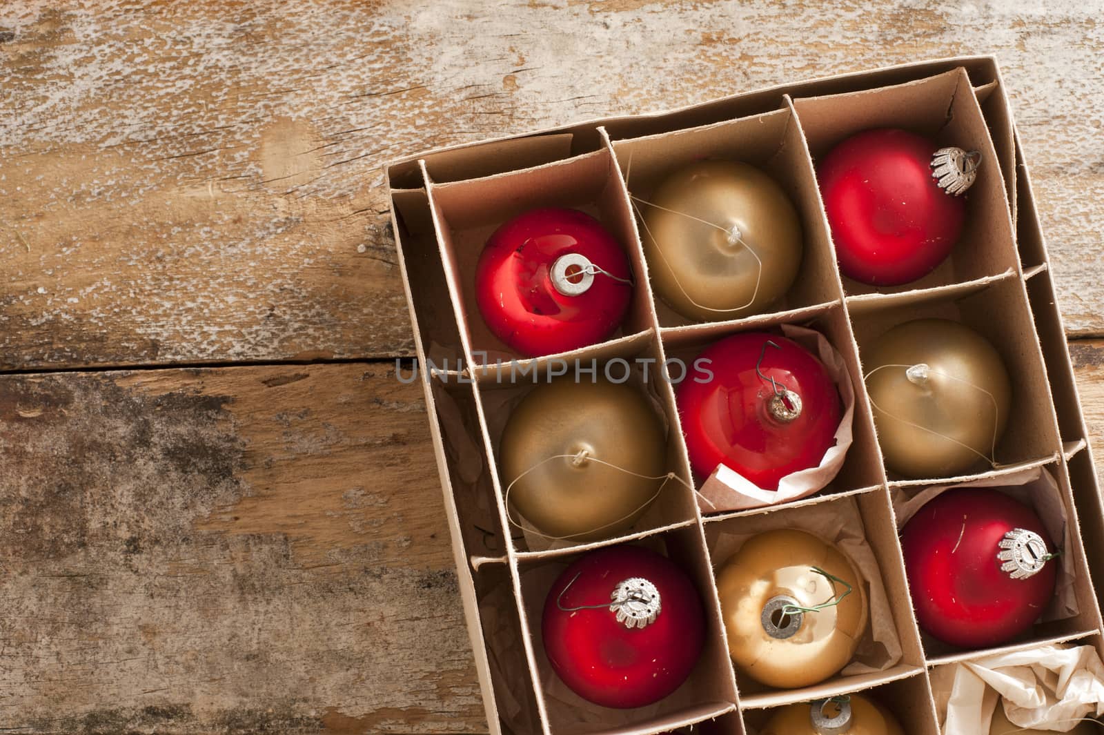 Shiny red and gold holiday ornaments in box on rustic table as seen from an overhead view