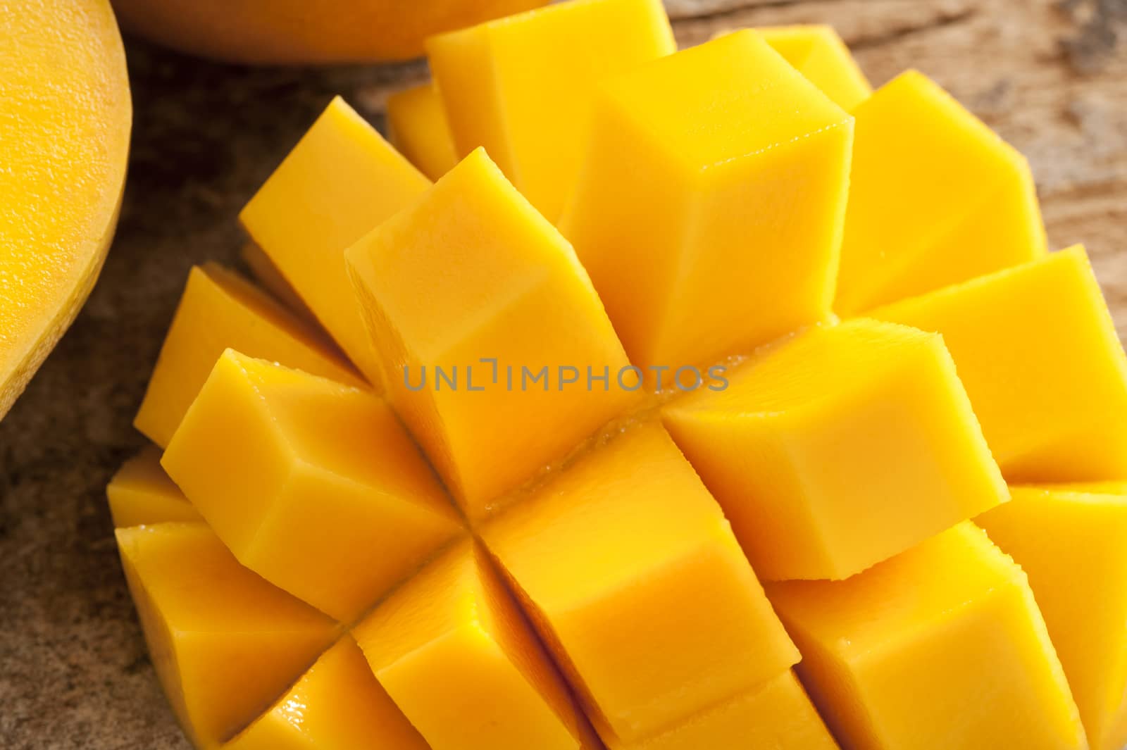 Delicious yellow mango peeled and cut into squares beside other ones on a wooden rustic table