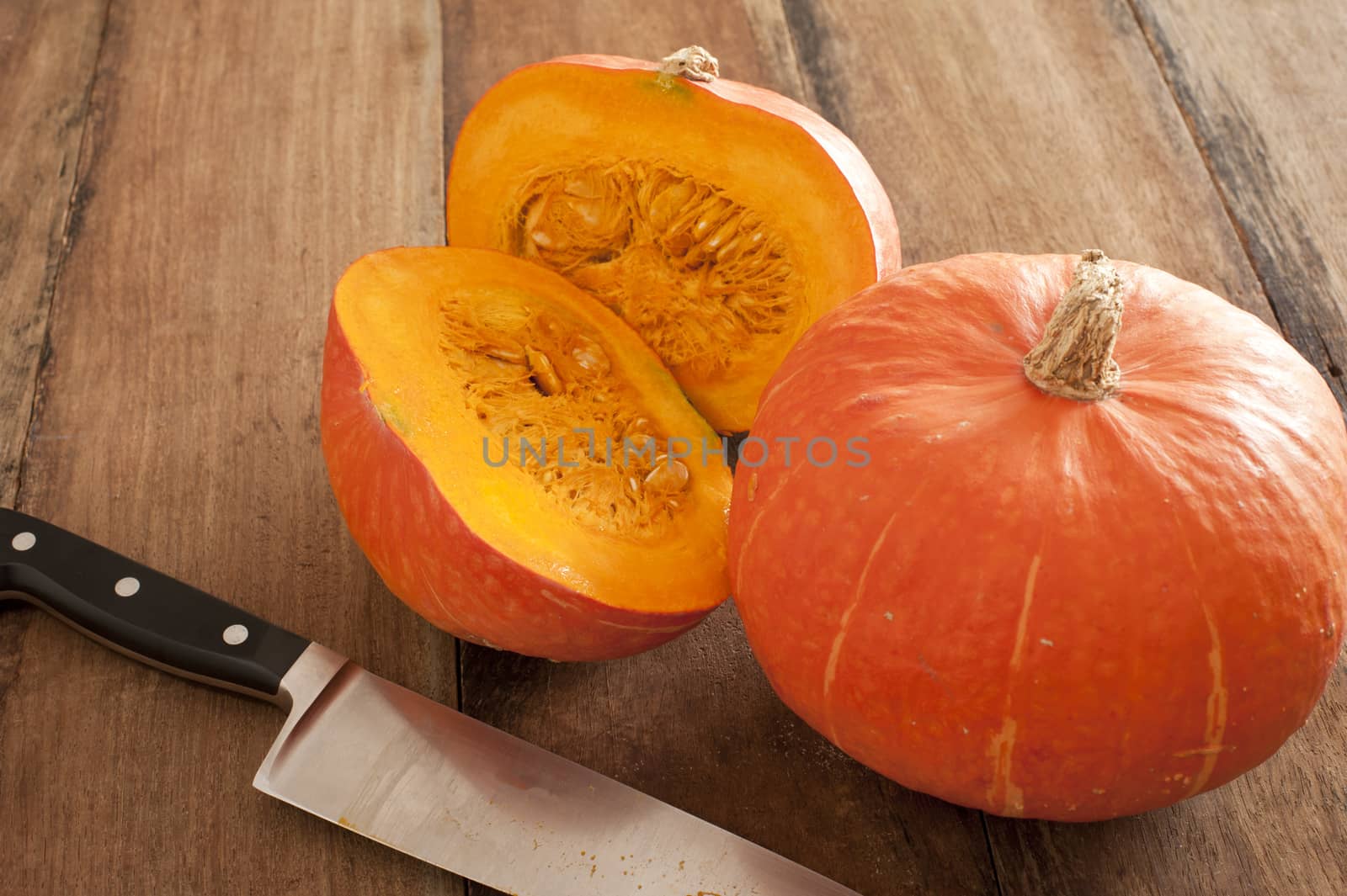 Small round oddly shaped pumpkin cut in middle beside bigger one and a large sharp knife