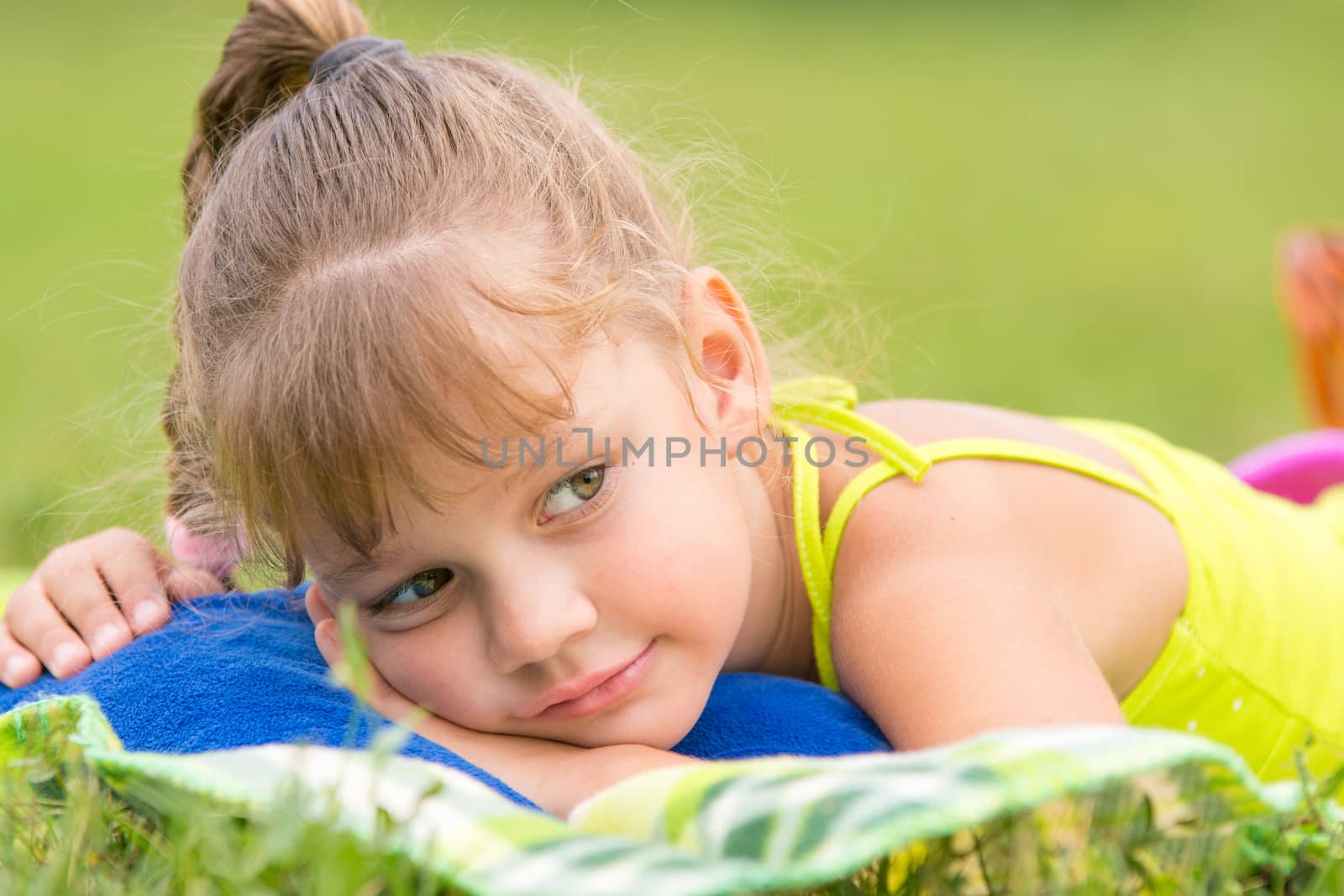 Five-year girl lies on a bed on a green meadow and thoughtfully looks aside