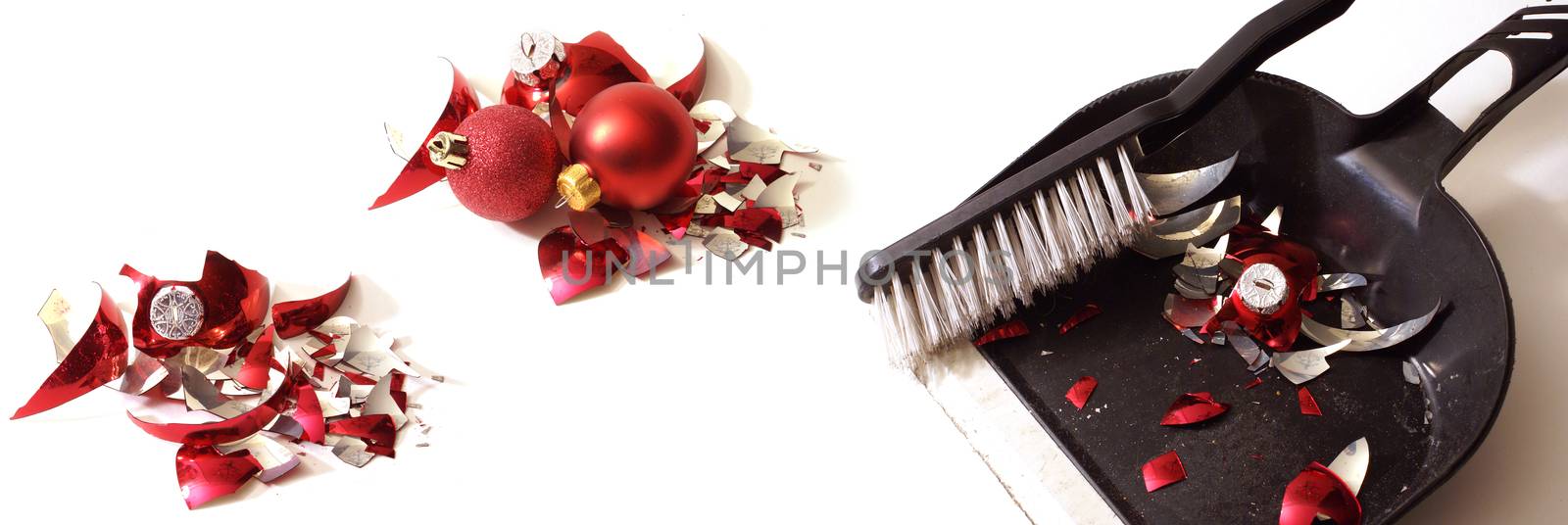 A smashed red holiday bauble has fallen to many pieces so a broom and dustpan come to clean up the mess.
