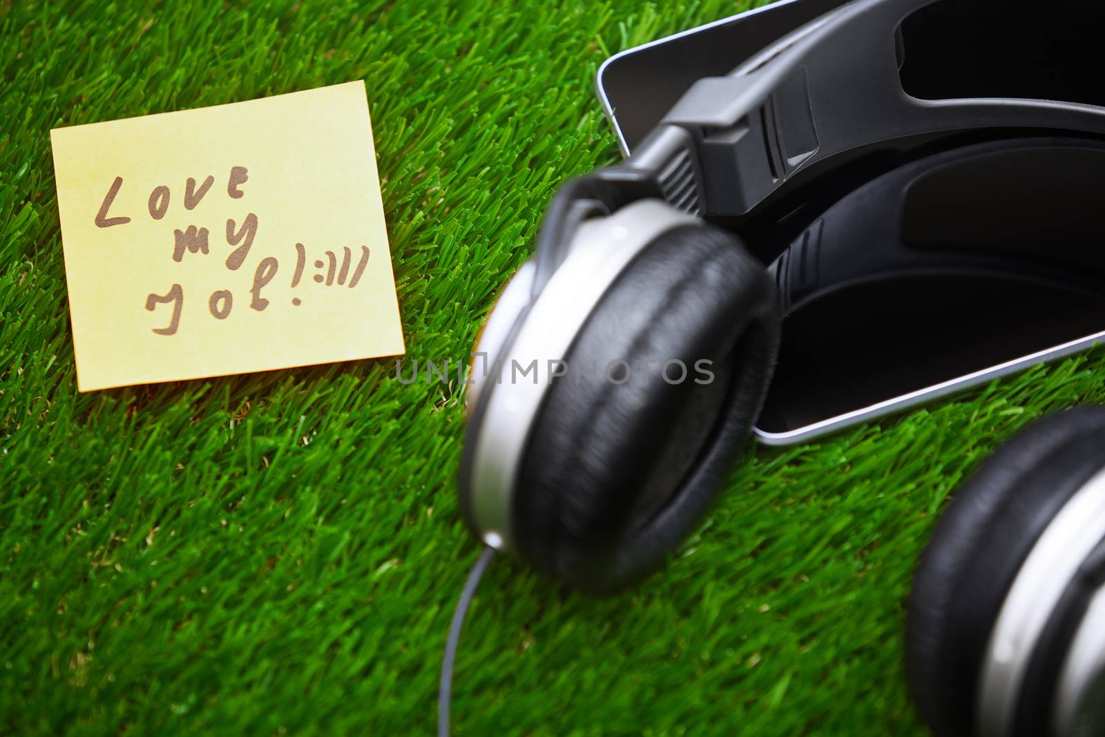 Text on sticky note on a grass with headphones and digital tablet