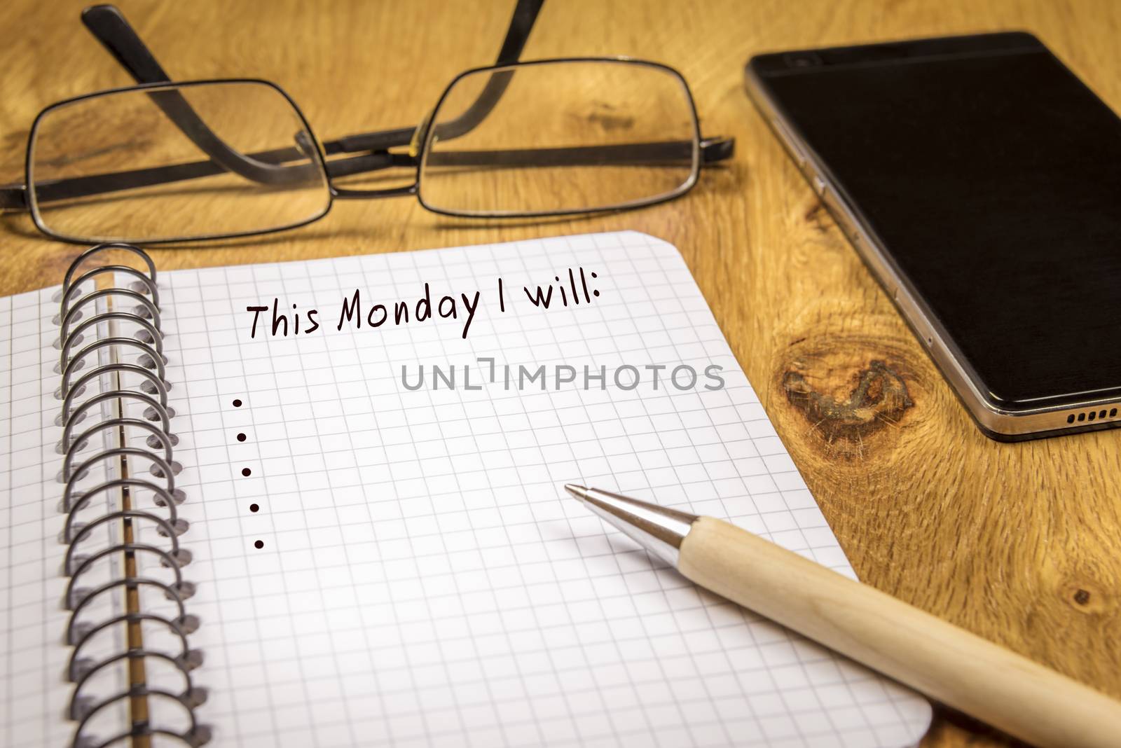 Conceptual image with organizing the plans for the beginning of the week, on a math spiral notebook. Eyeglasses, a pen and a phone are in the background.