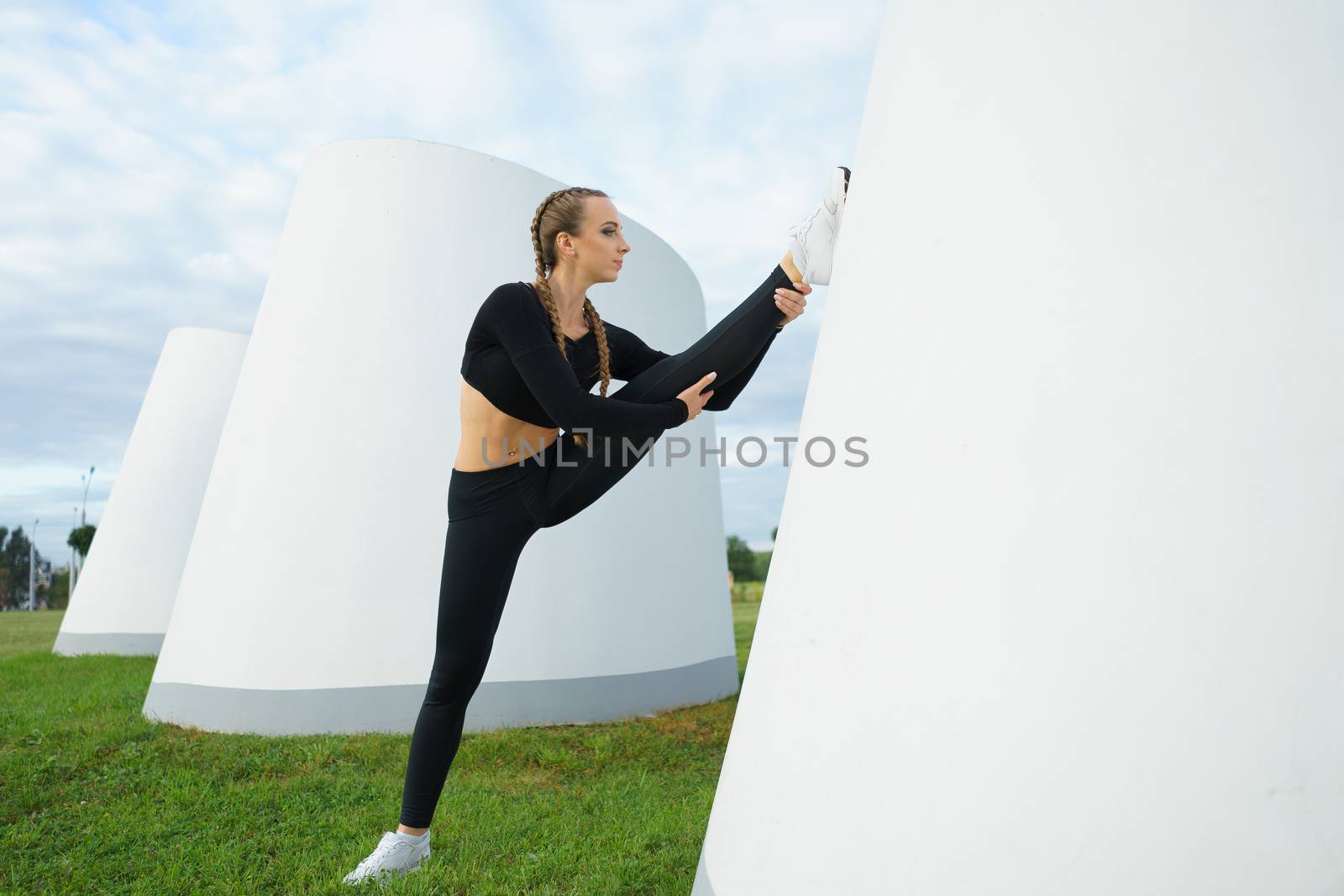 Concept: healthy lifestyle, sport. Attractive happy girl fitness trainer stretch outdoor workout at modern downtown urban area during sunset.