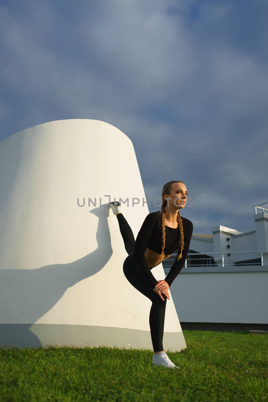 Happy girl stretch outdoor at modern urban area during sunset by mrakor