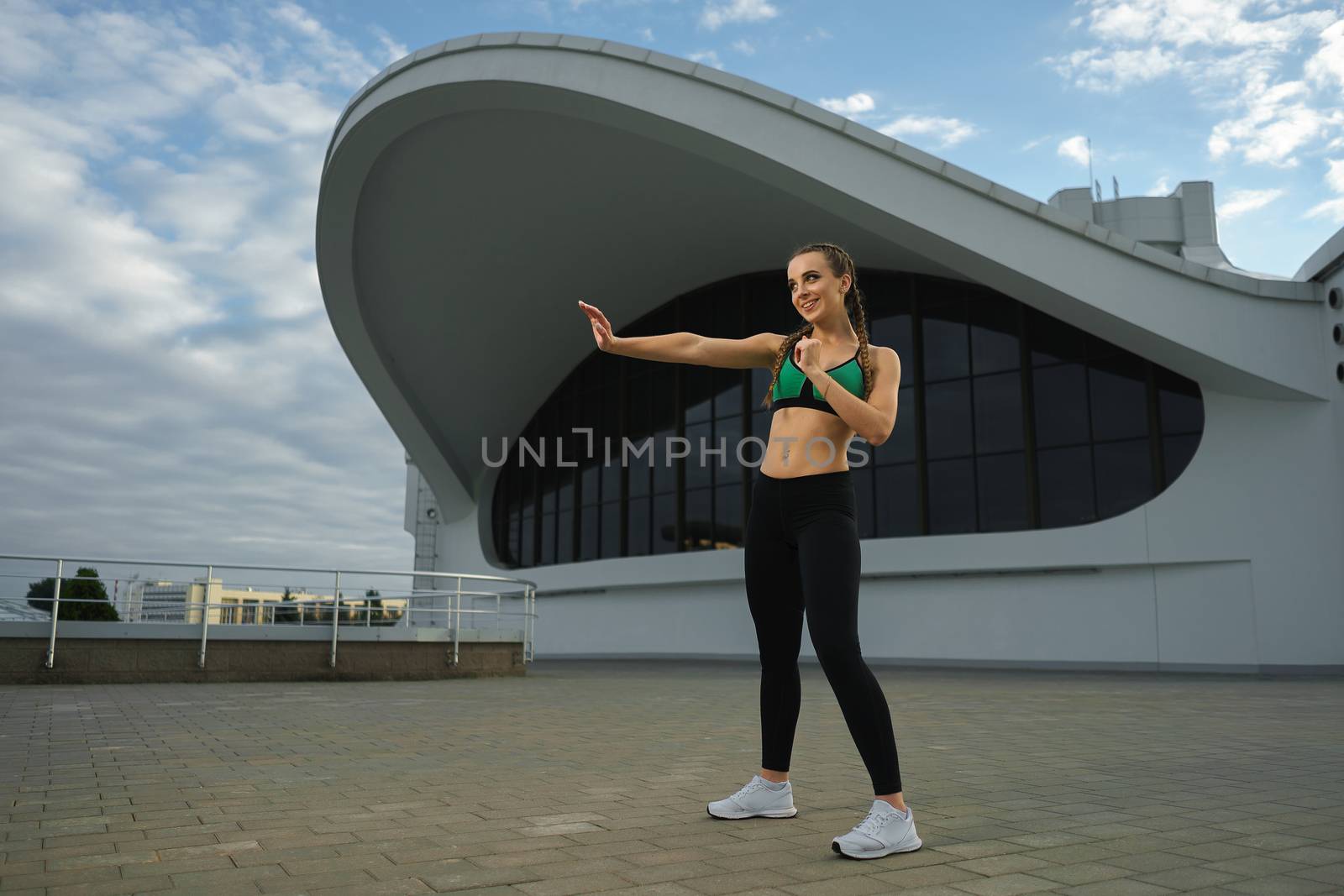 Concept: healthy lifestyle, sport. Attractive happy girl fitness trainer do outdoor workout at modern downtown urban area during sunset.