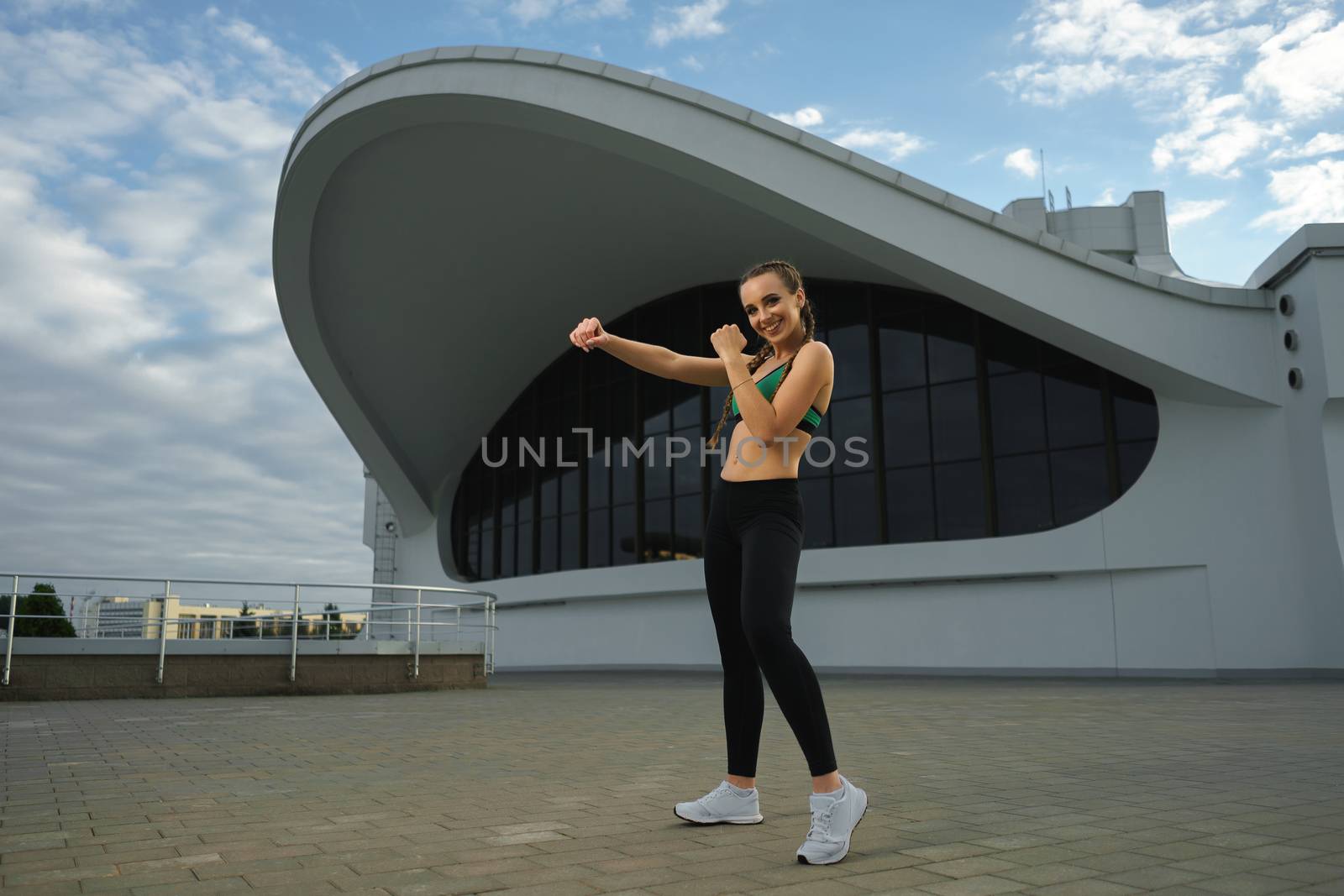 Concept: healthy lifestyle, sport. Attractive happy girl fitness trainer do outdoor workout at modern downtown urban area during sunset.