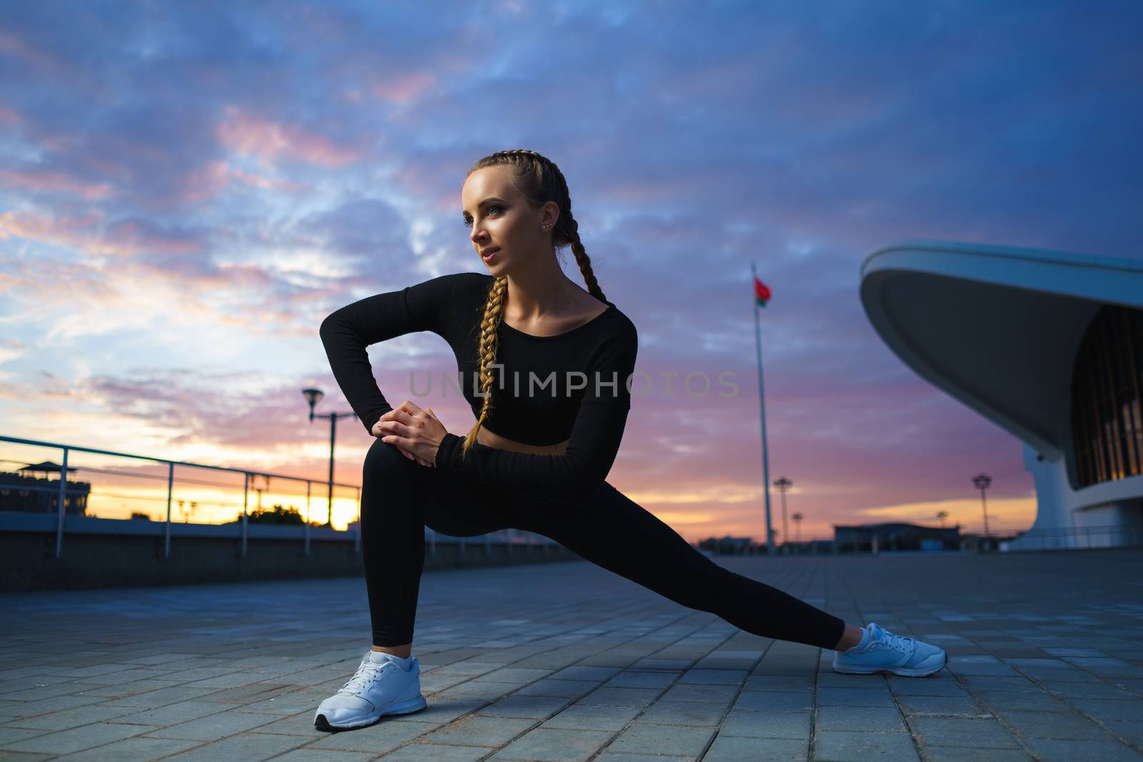 Concept: healthy lifestyle, sport. Attractive happy girl fitness trainer stretch outdoor workout at modern downtown urban area during sunset.