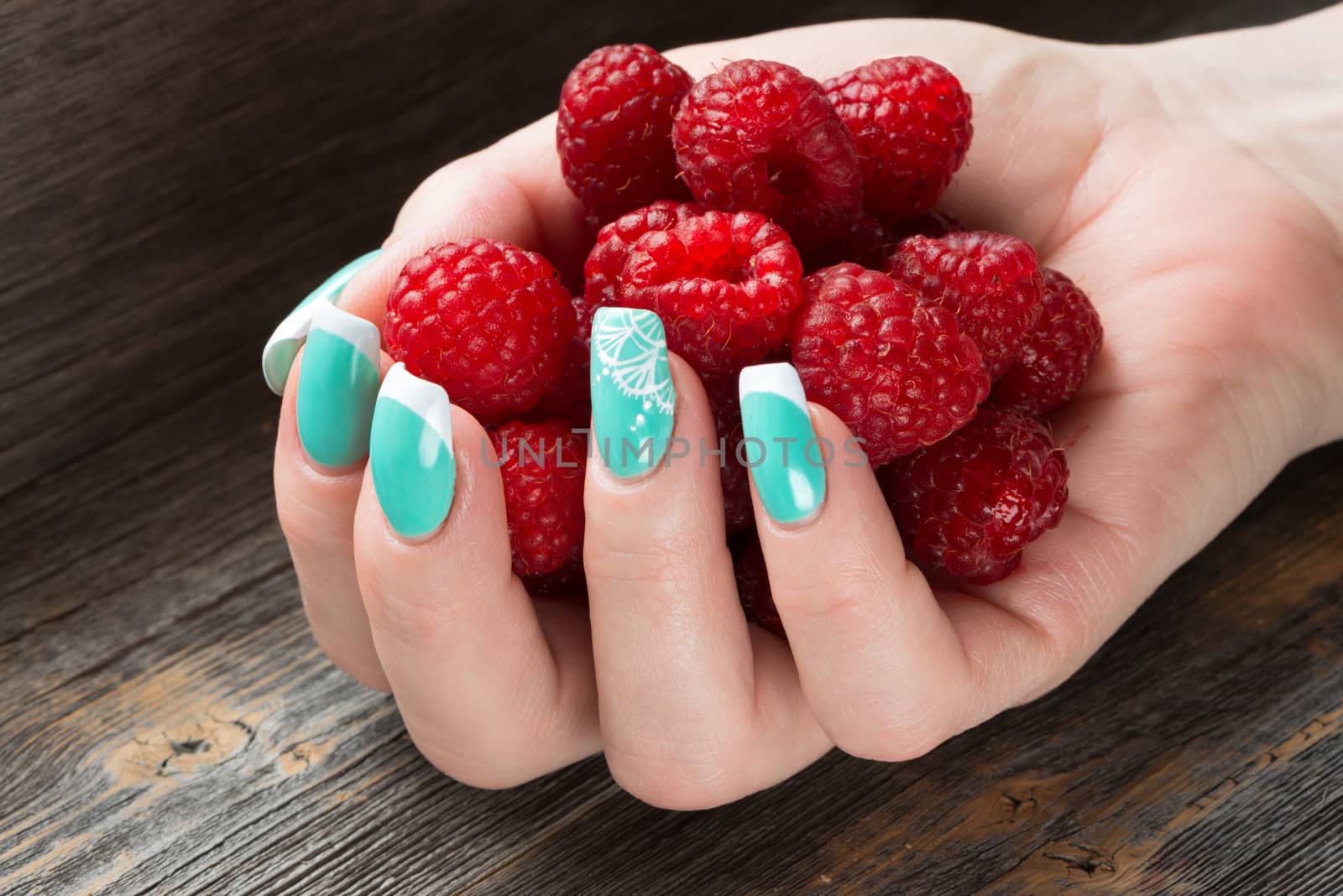 The female hand holds a handful of ripe berries  raspberry against the background   wooden table by fotooxotnik