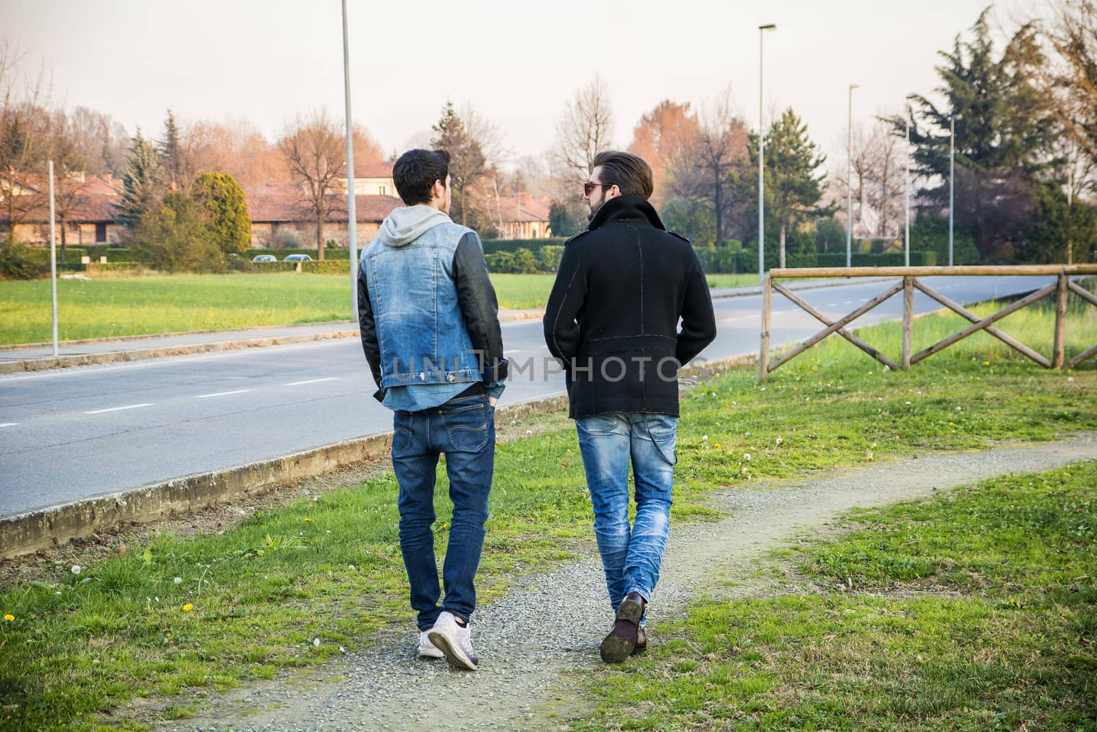 Two handsome casual trendy young men, 2 friends, in an urban park walking and chatting together