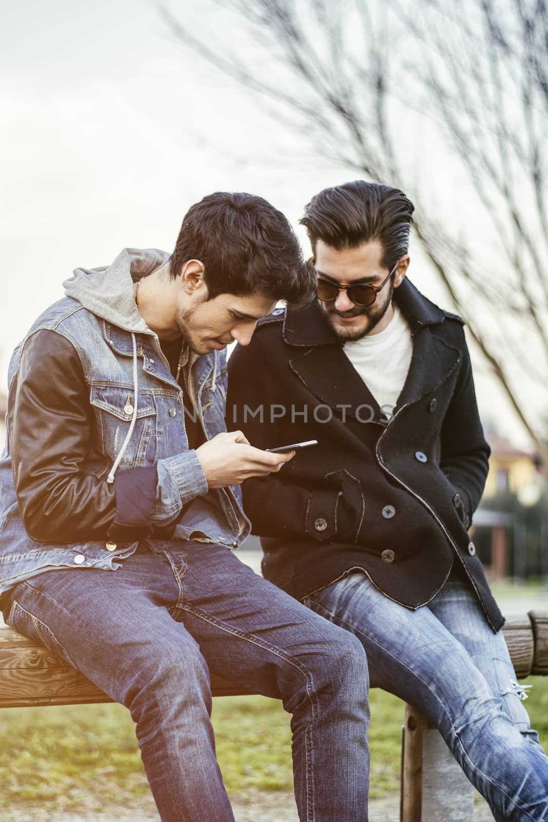 Two young men sitting reading sms text message by artofphoto