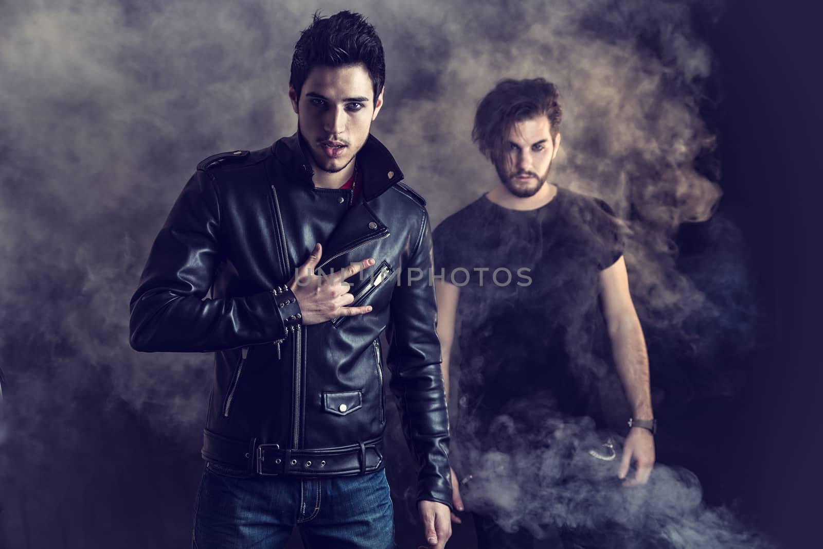 Two attractive young hard rock men posing in studio. Black background