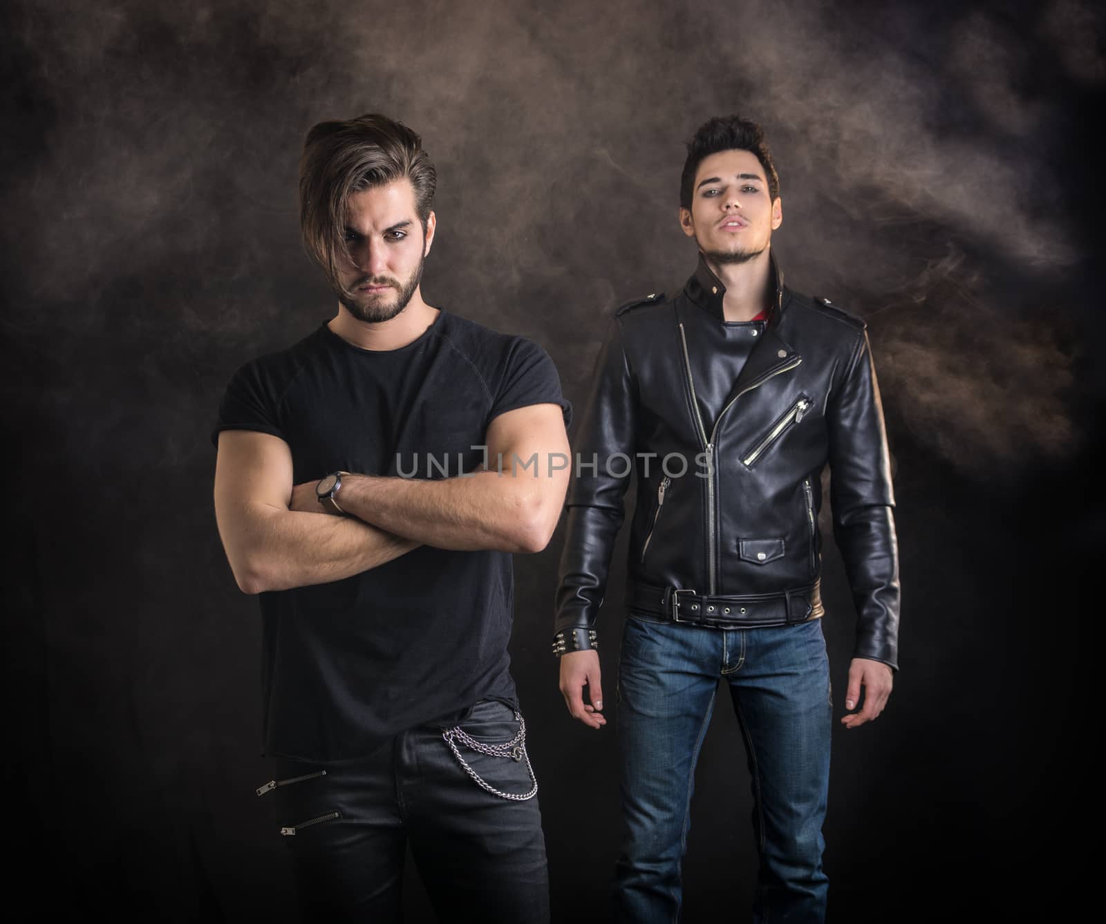 Two attractive young hard rock men posing in studio. Black background