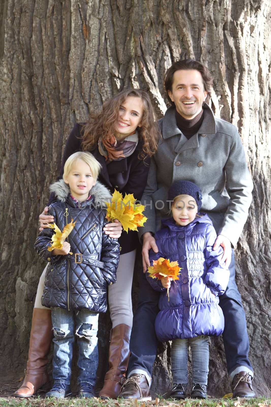 Happy family in autumn park near big tree trunk