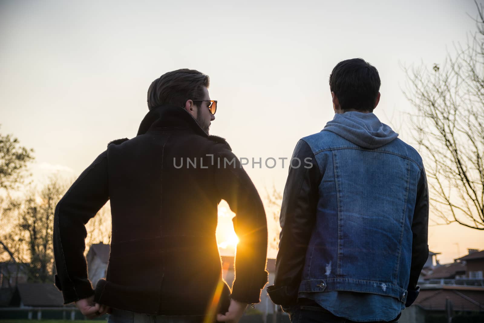 Two handsome casual trendy young men, 2 friends, in an urban park walking and chatting together