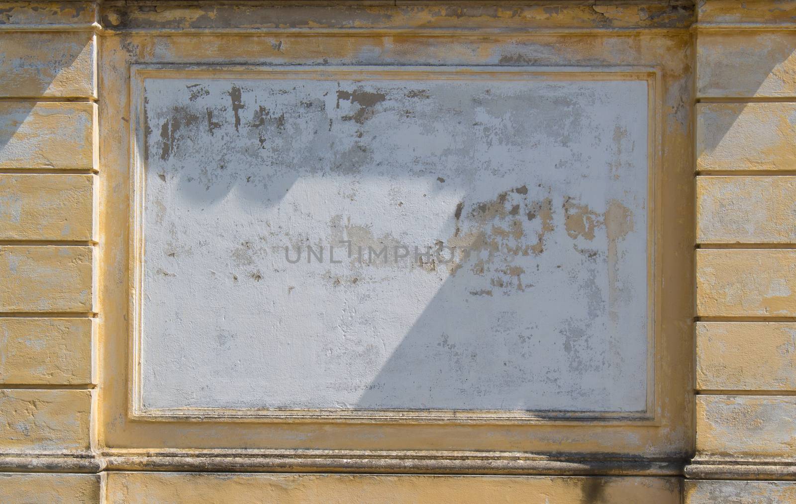 Detail of a facade creating a white area framed by yellow ornate wall. Weathered surface of the old wall.