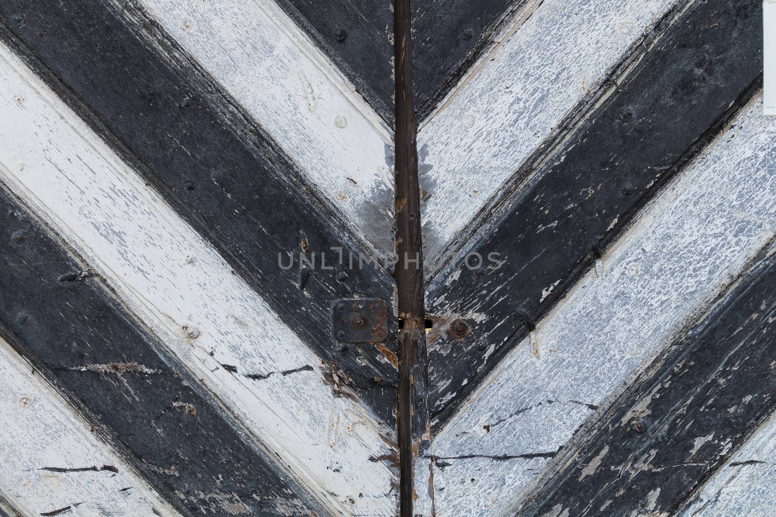 Detail of an old wooden gate with black and white stripes, creating a letter "V" or an arrow.