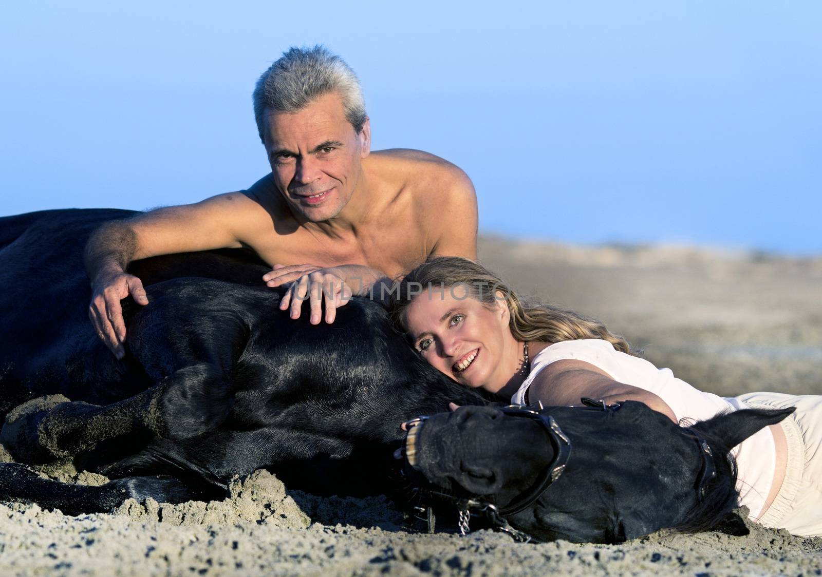 lovers and their black stallion lying down on the beach
