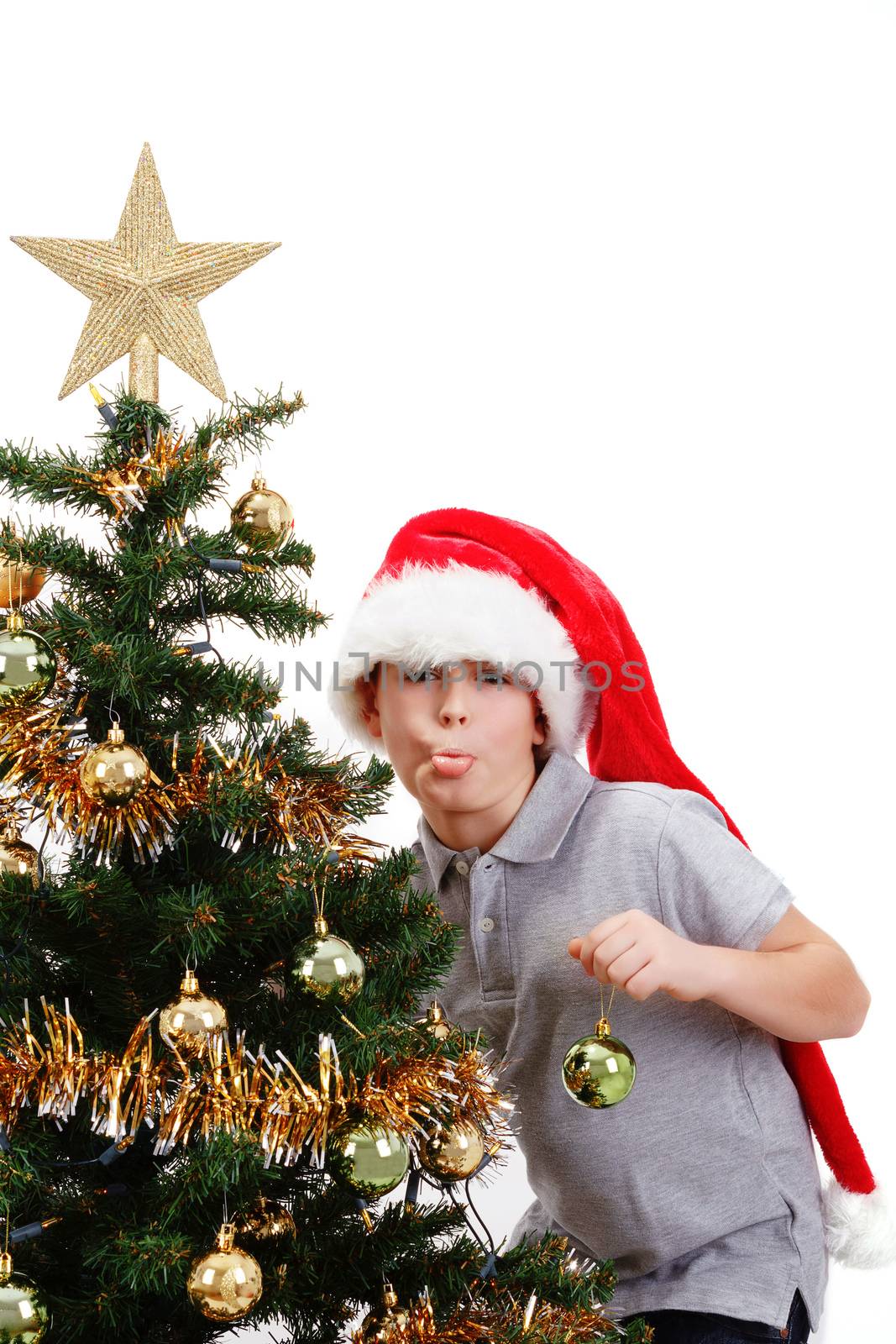 Boy with santa hat sticking out tongue at  the Christmas tree on white background
