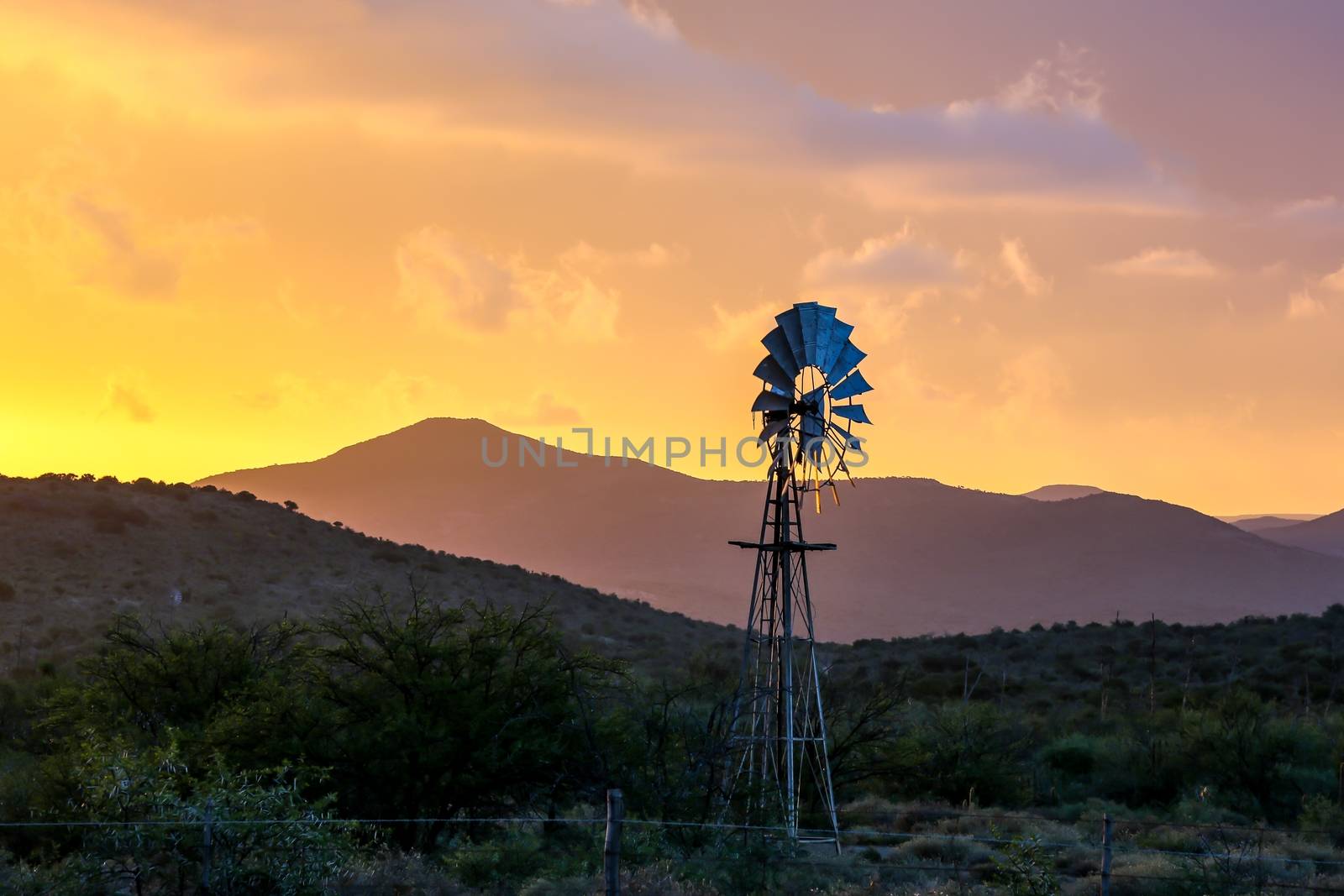 Water Pump Windmill on Arid Farmland at Sunset by fouroaks