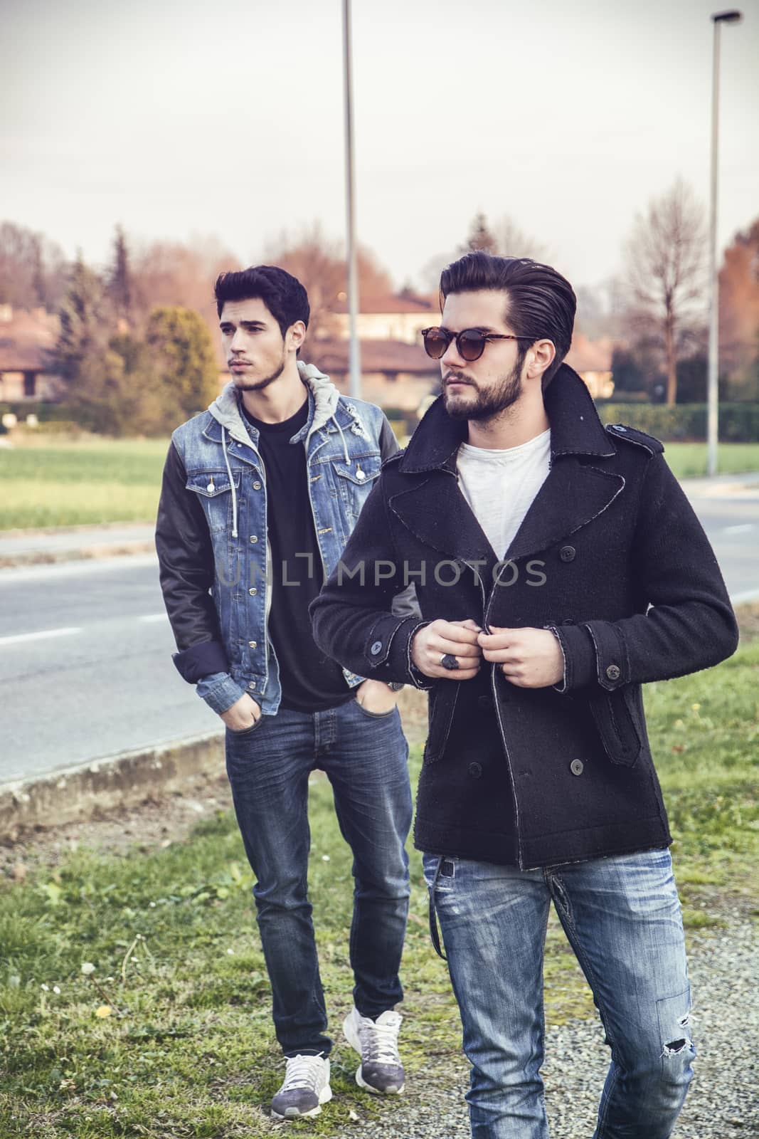 Two handsome casual trendy young men, 2 friends, in an urban park walking and chatting together