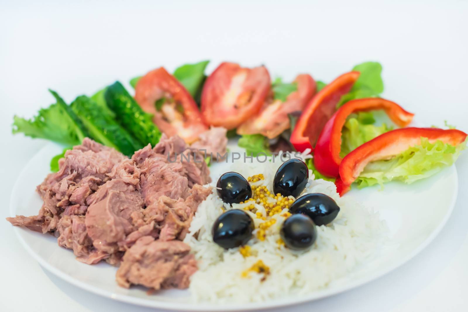 rice tuna chopped vegetables and olives in a white plate on a white background