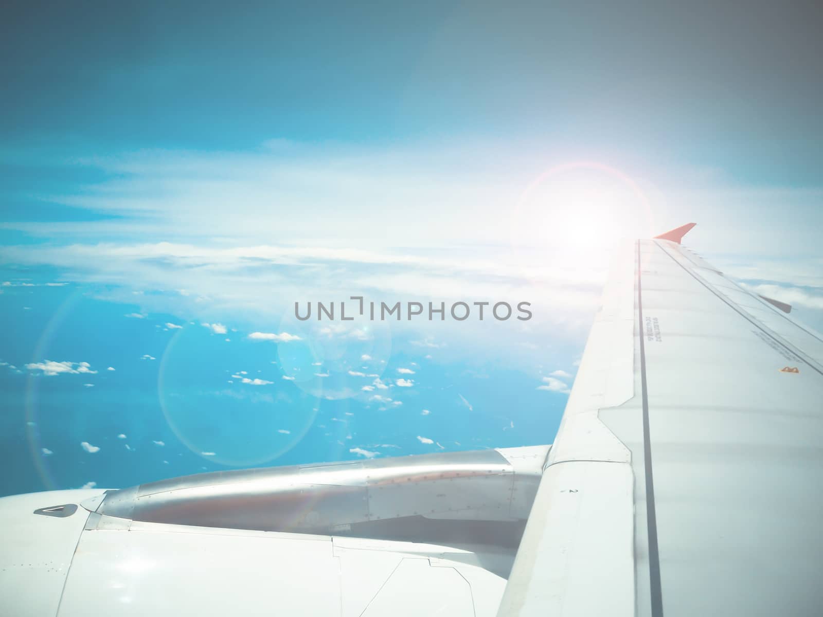 Lens flare and view of jet plane wing with cloud patterns by worrayuth