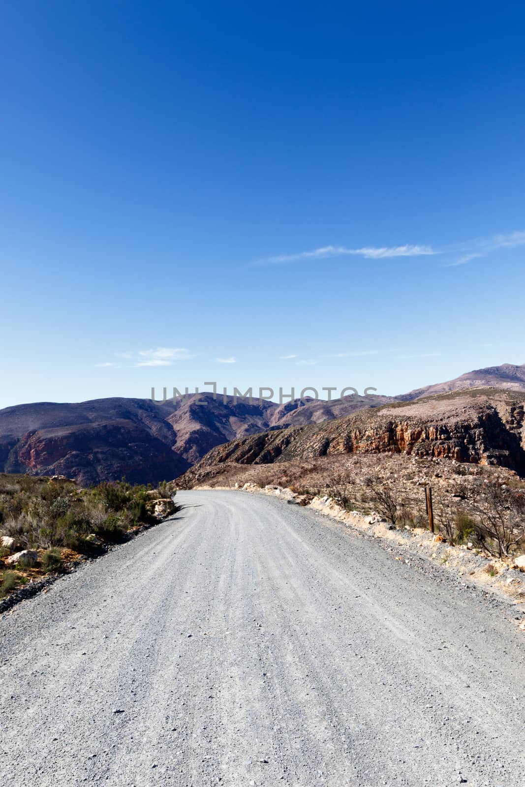 Gravel road leading to the mountains with blue skies and some clouds