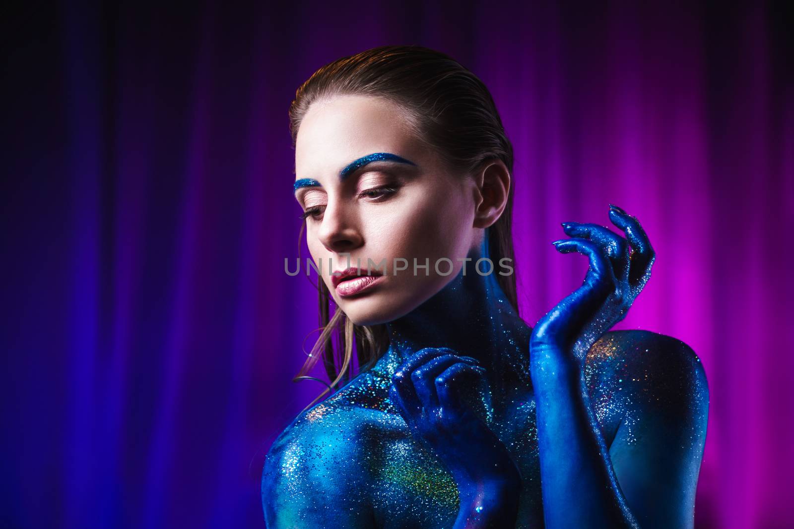 Portrait of an beautiful woman painted with purple cosmic colors and spangled. Body art project. Concept: fashion, makeup, extraordinary.