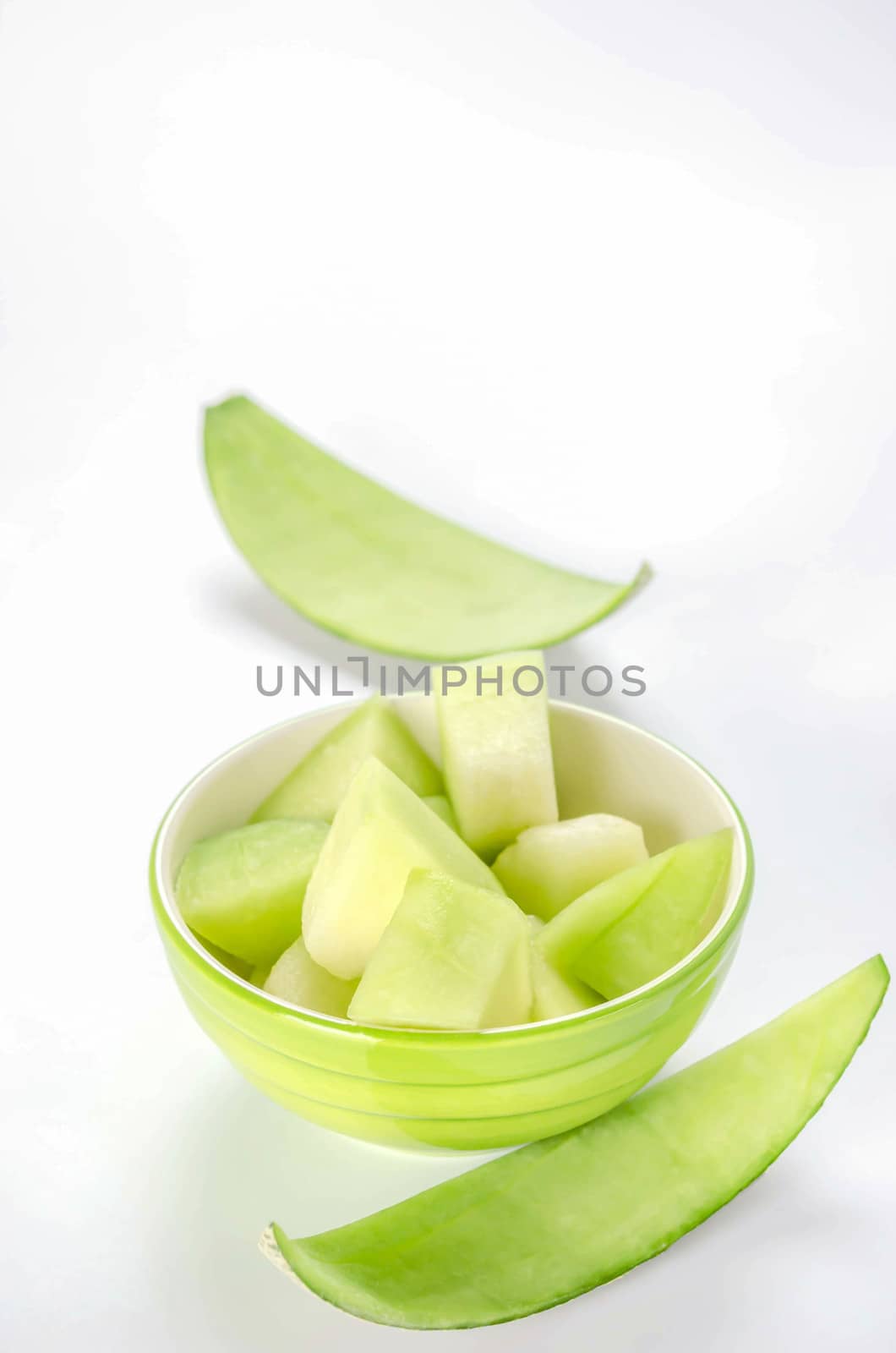 shopped green melon in bowl on white background
