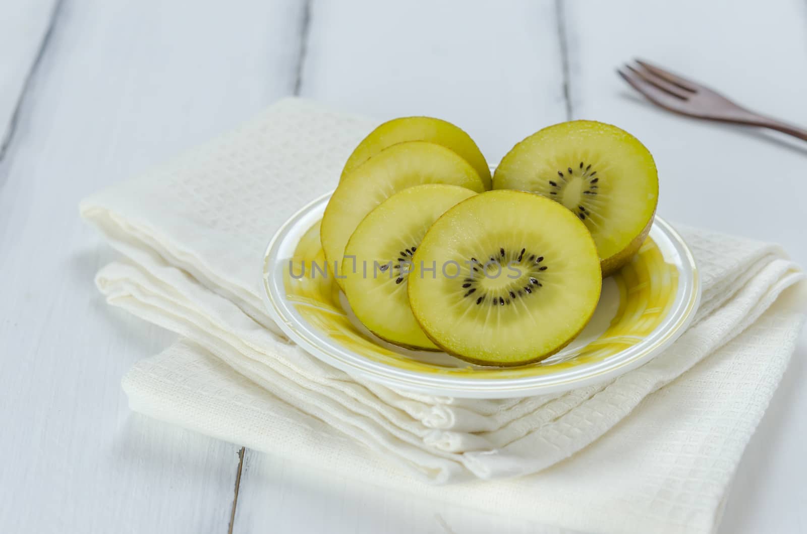golden kiwi fruit and sliced on dish over white wooden background