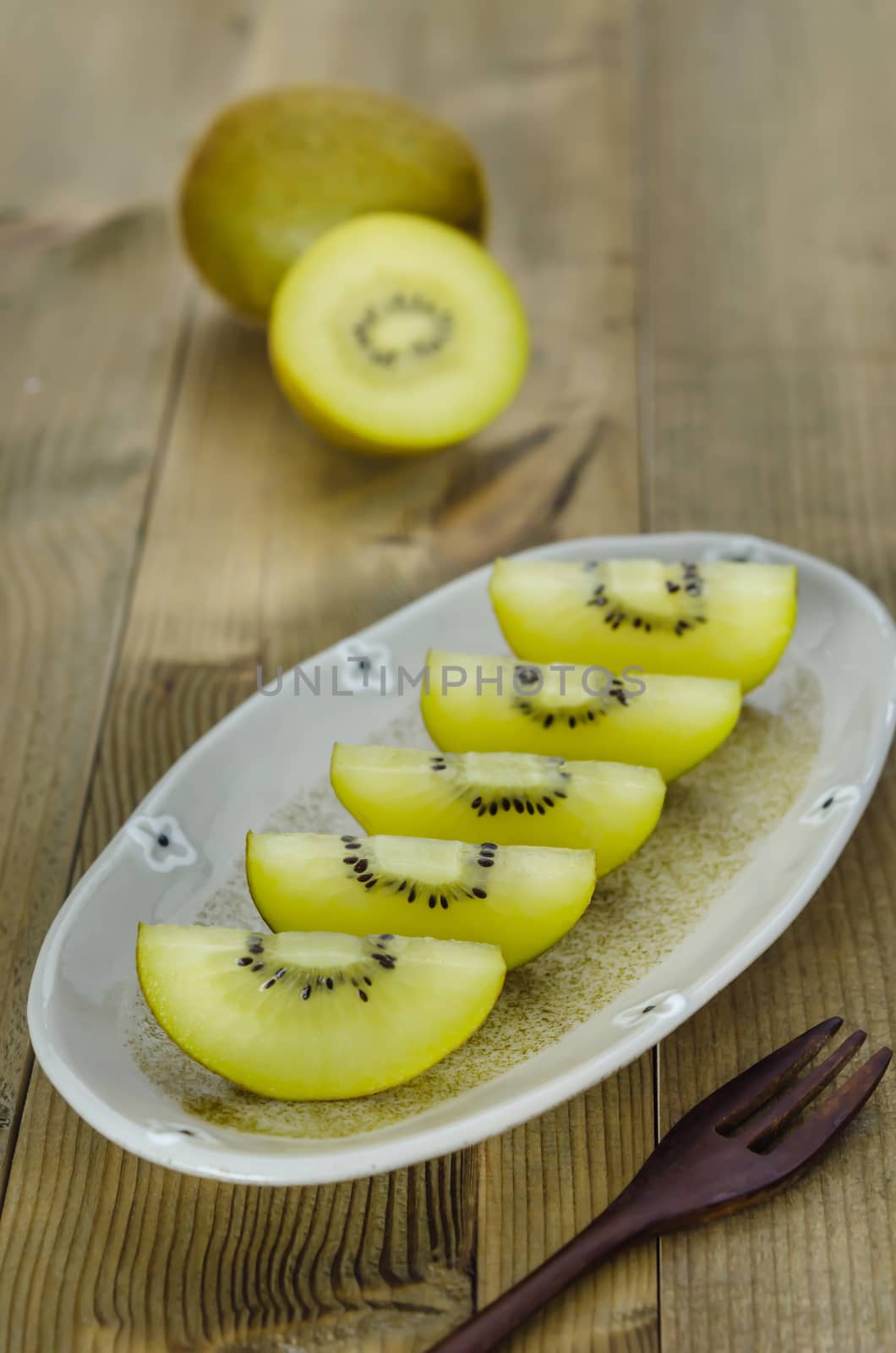 golden kiwi fruit and sliced on dish over wooden background