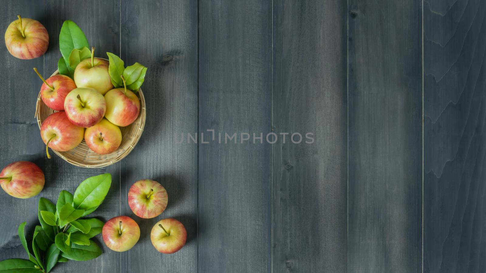 Top view red and yellow apple with leaves and  bamboo basket on wooden background with free space for text